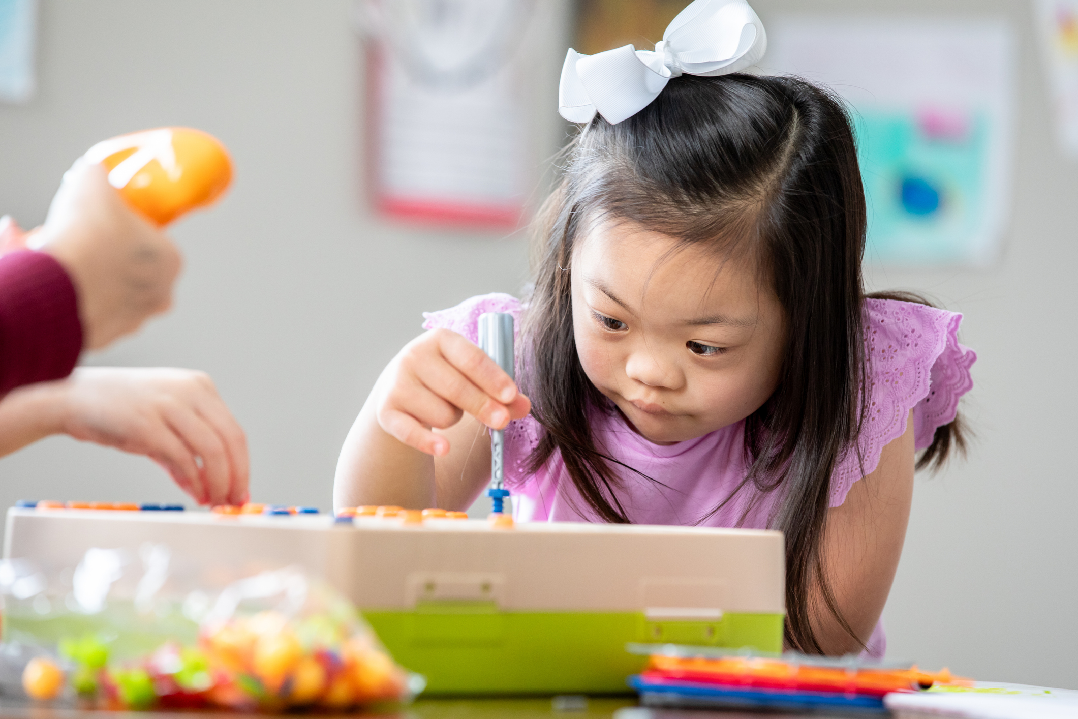 Little girl with Down Syndrome concentrates while using STEM educational building toy in special education classroom