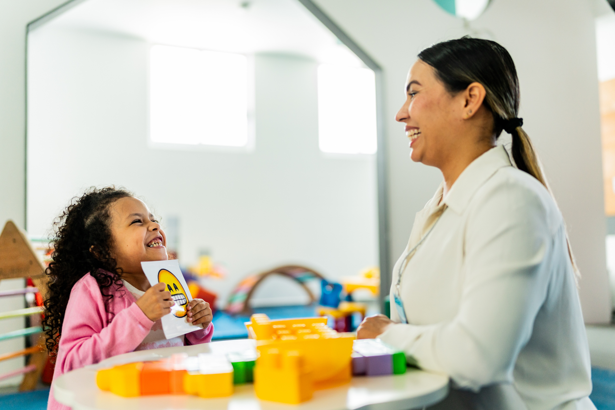 Mid adult therapist woman playing boards with child girl during therapy at clinic