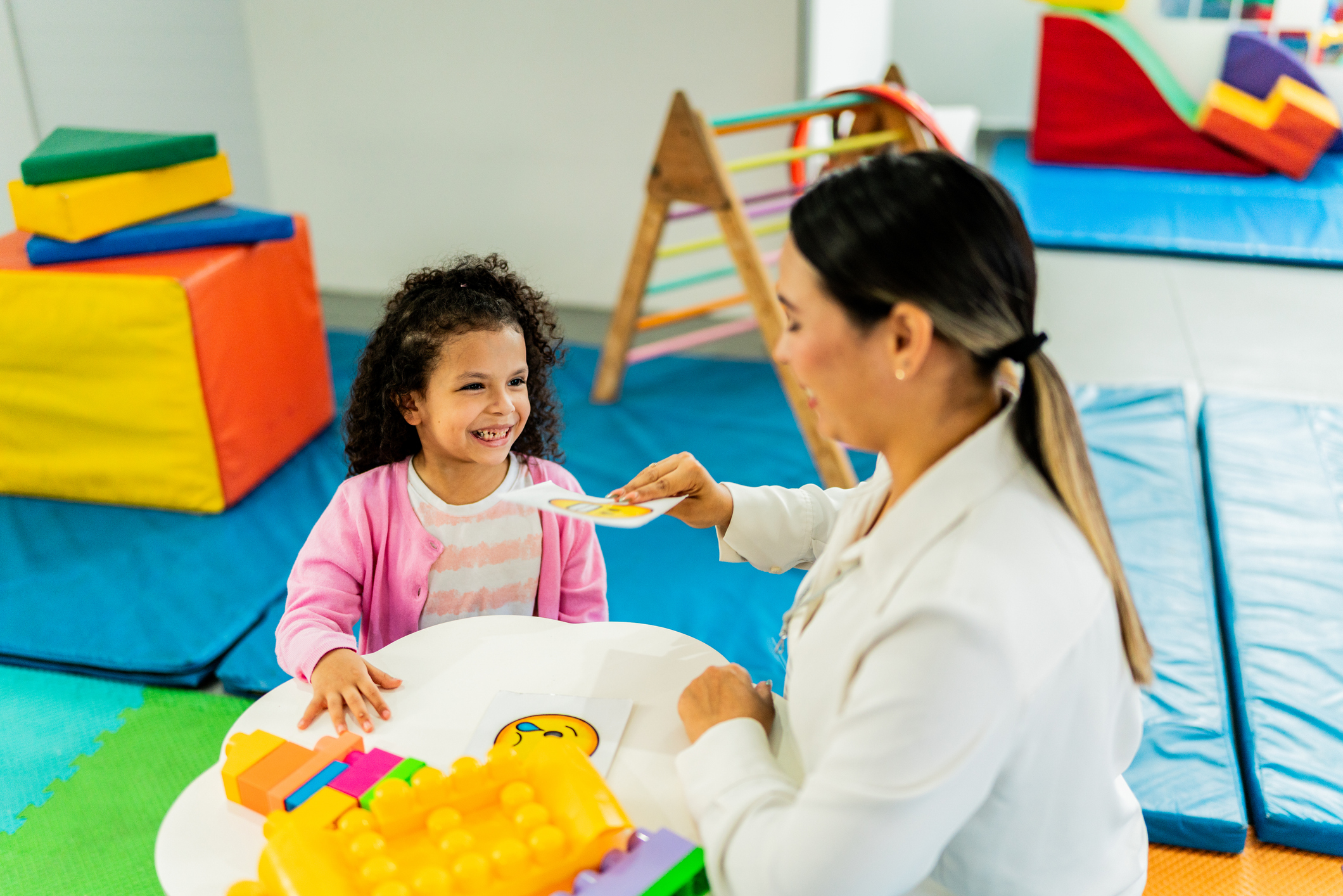 Mid adult therapist woman playing boards with child girl during therapy at clinic