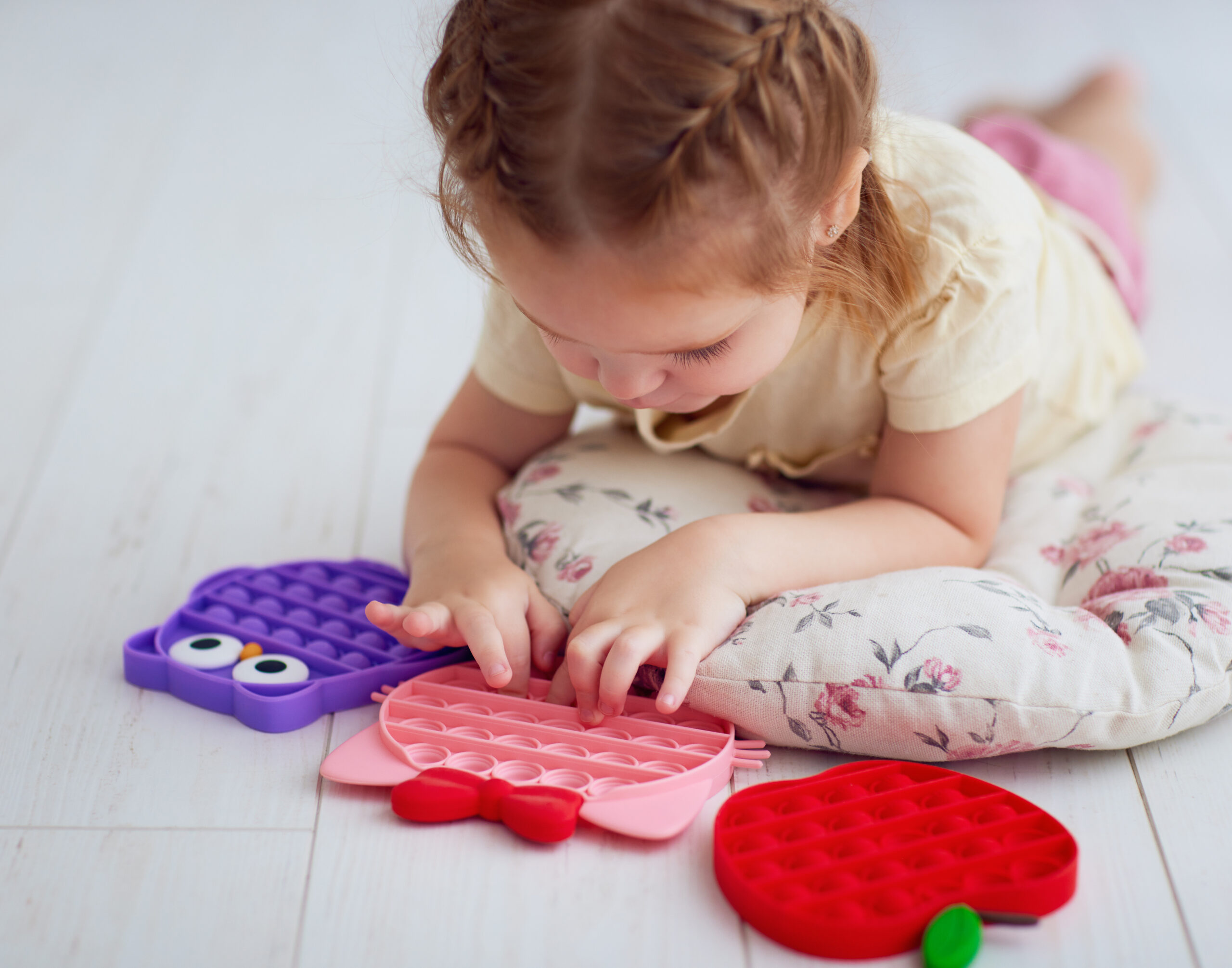 happy baby girl playing with colorful sensory toys. pushing the bubles on pop it fidget toy