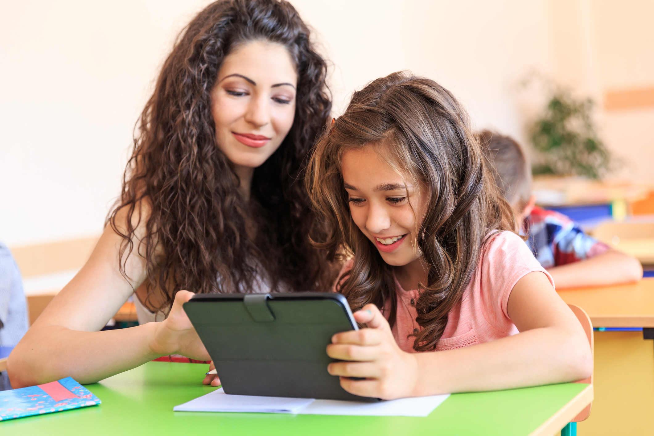 Teacher helping schoolgirl using a tablet computer in class